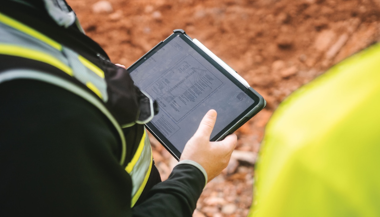 Nahaufnahme von einem Tablet, das eine Person mit Baustellenbekleidung in der Hand hält.