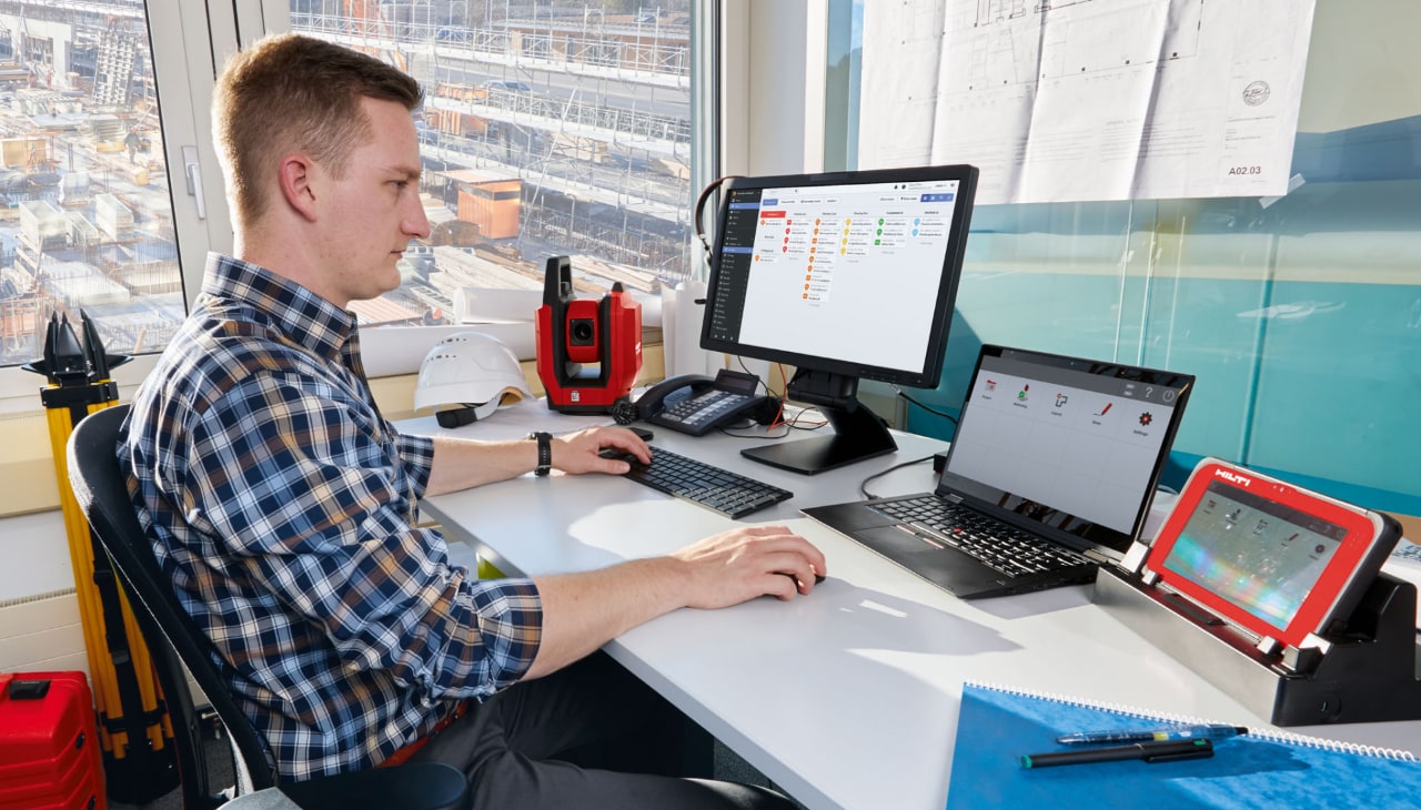Mann sitzt im Büro vor seinem PC und arbeitet, auf einem Bildschirm hat er das Programm Fieldwire geöffnet.