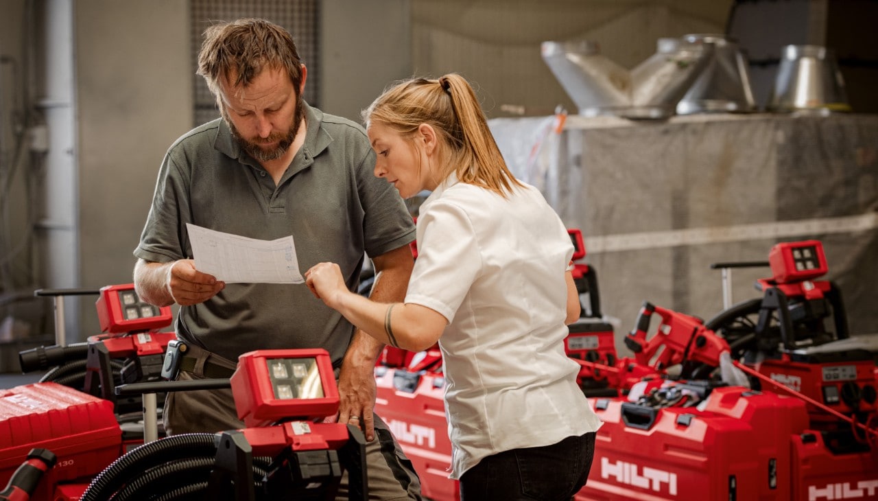 Eine Hilti Mitarbeiterin und ein Kunde prüfen Hilti Geräte in einer Werkstatt.