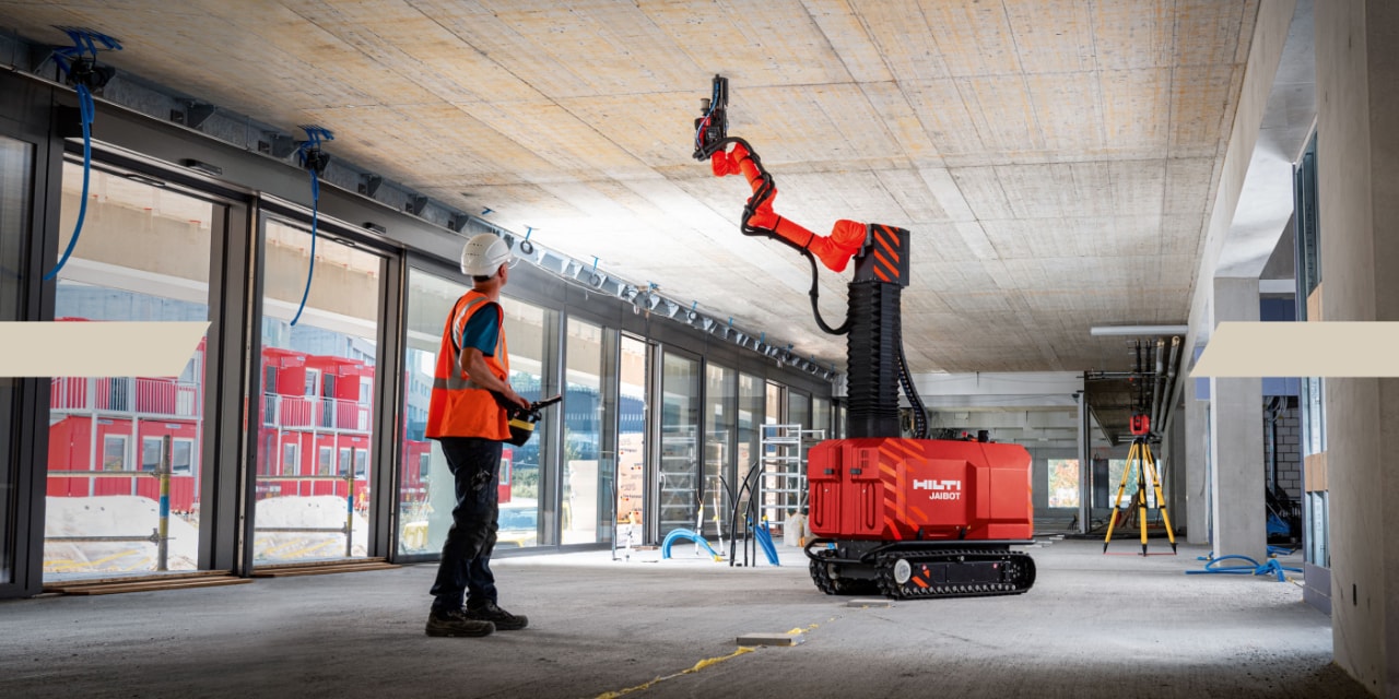 Ein Mann lässt den Hilti Jaibot Arbeiten an der Decke vornehmen, indem er diesen über eine Fernsteuerung bedient. 