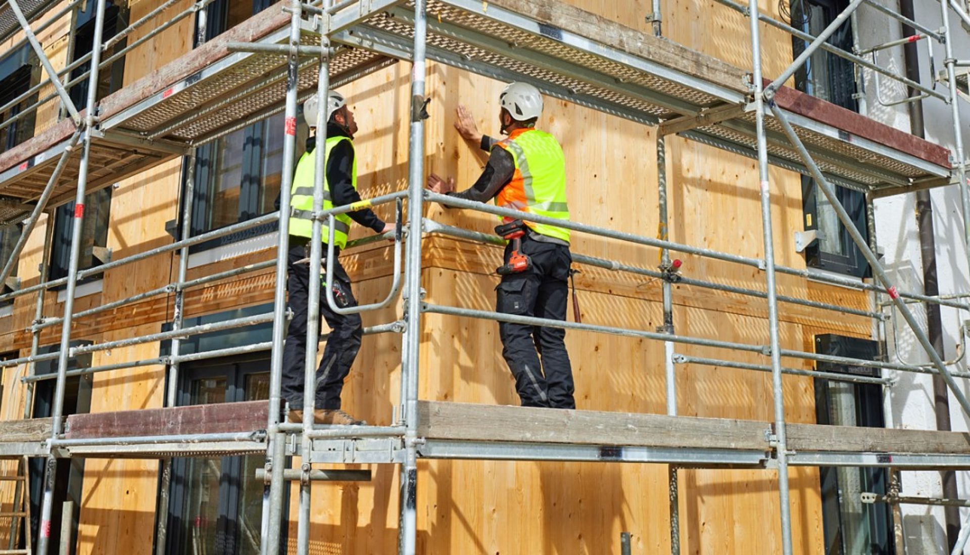 zwei Arbeiter auf einem Gerüst vor einer vorgehängten hinterlüfteten Holzfassade