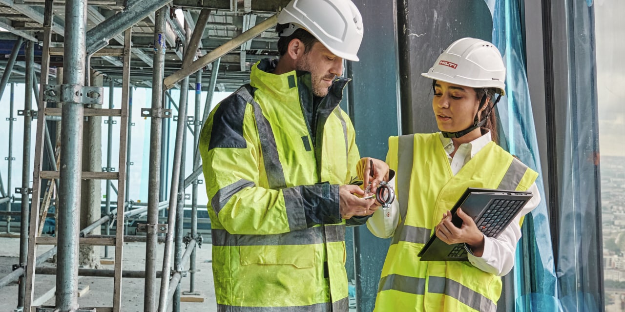 Aussendienstmitarbeiterin spricht mit einem Kunden auf der Baustelle und zeigt ihm das MEP-Sortiment an Verbrauchsmaterialien 