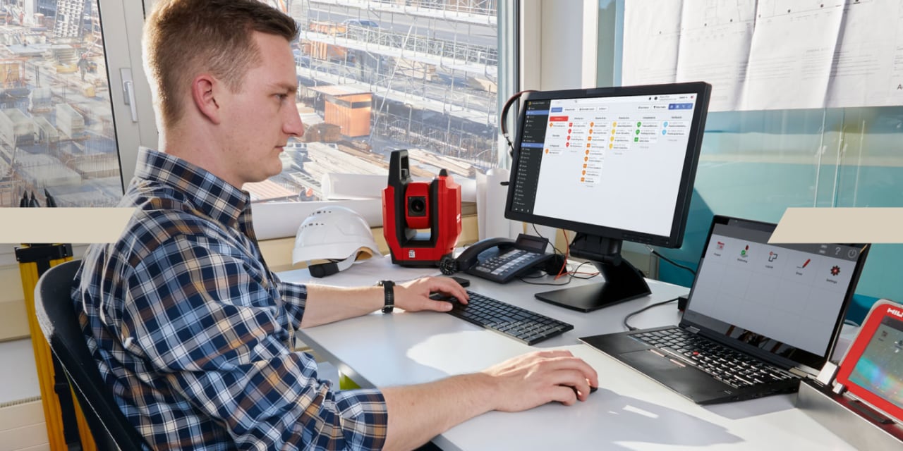 Un homme est assis dans le bureau devant son PC et travaille ; il ouvre le programme Fieldwire sur un écran.