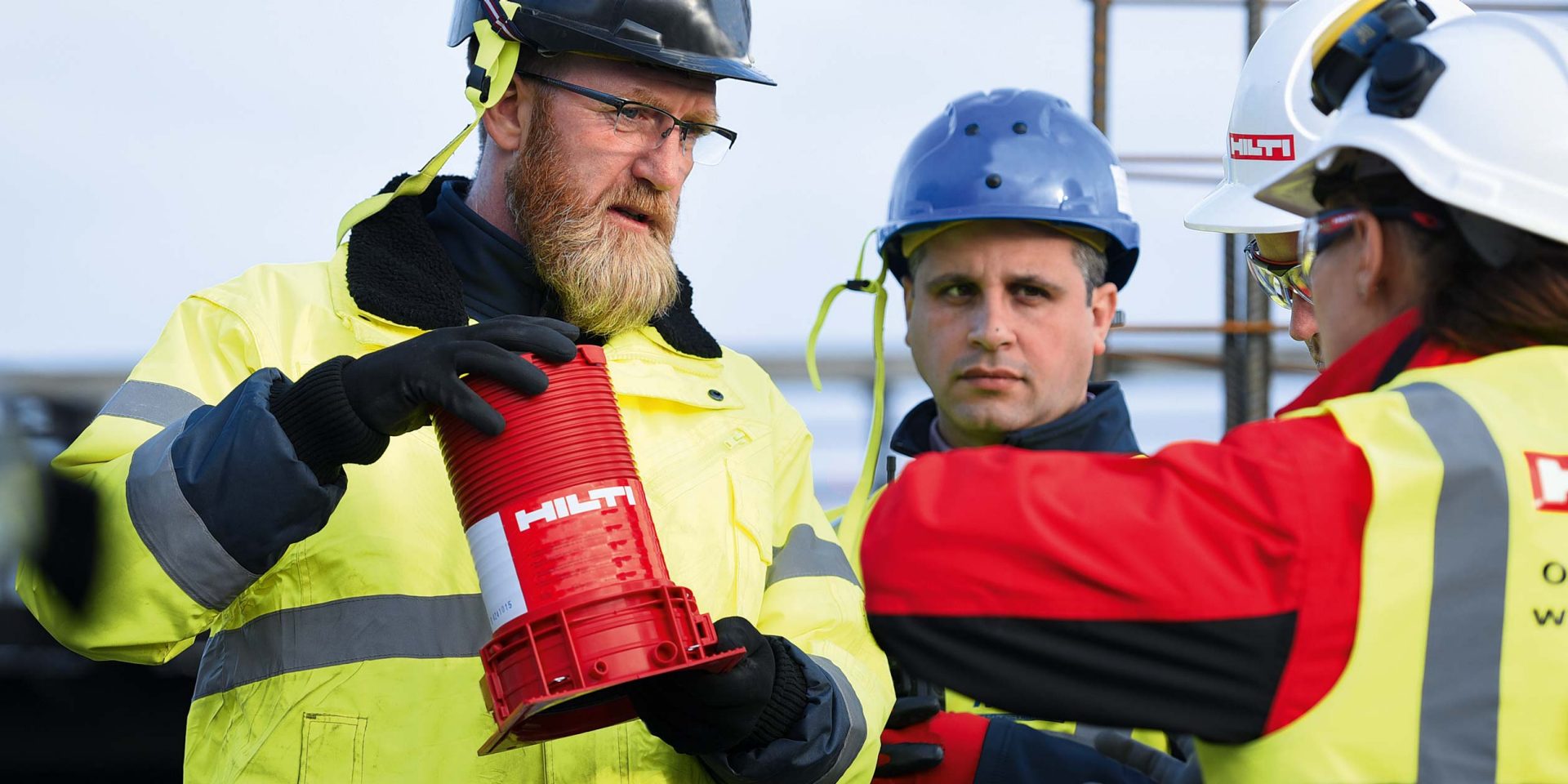 Un ouvrier du bâtiment et un contremaître ou un chef de chantier en conversation, un produit de protection contre l'incendie Hilti est tenu dans leurs mains.