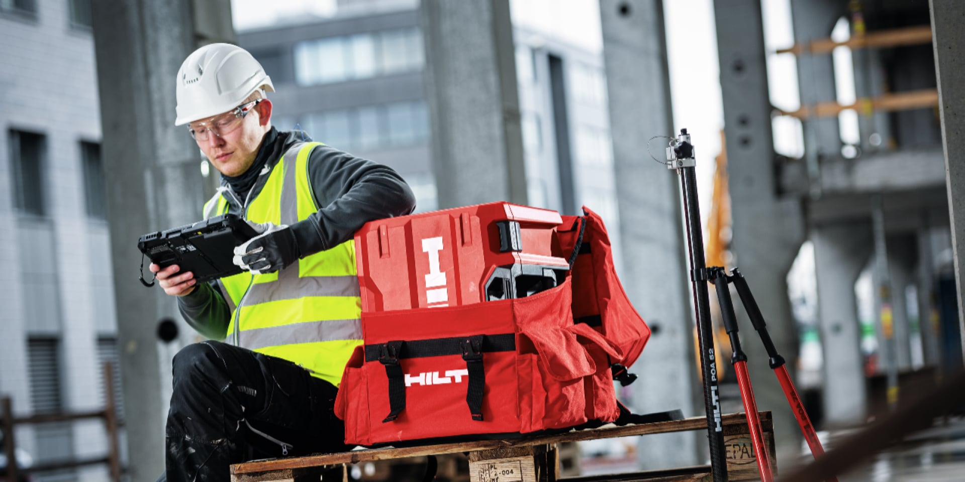 Une personne en tenue de travail regarde une tablette devant le coffret Hilti.