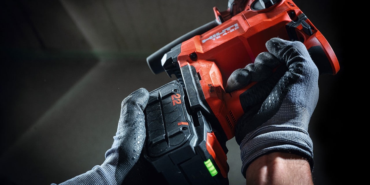 Una persona con guanti da lavoro applica una batteria agli ioni di litio Nuron a un perforatore a batteria Hilti TE 4-A22.