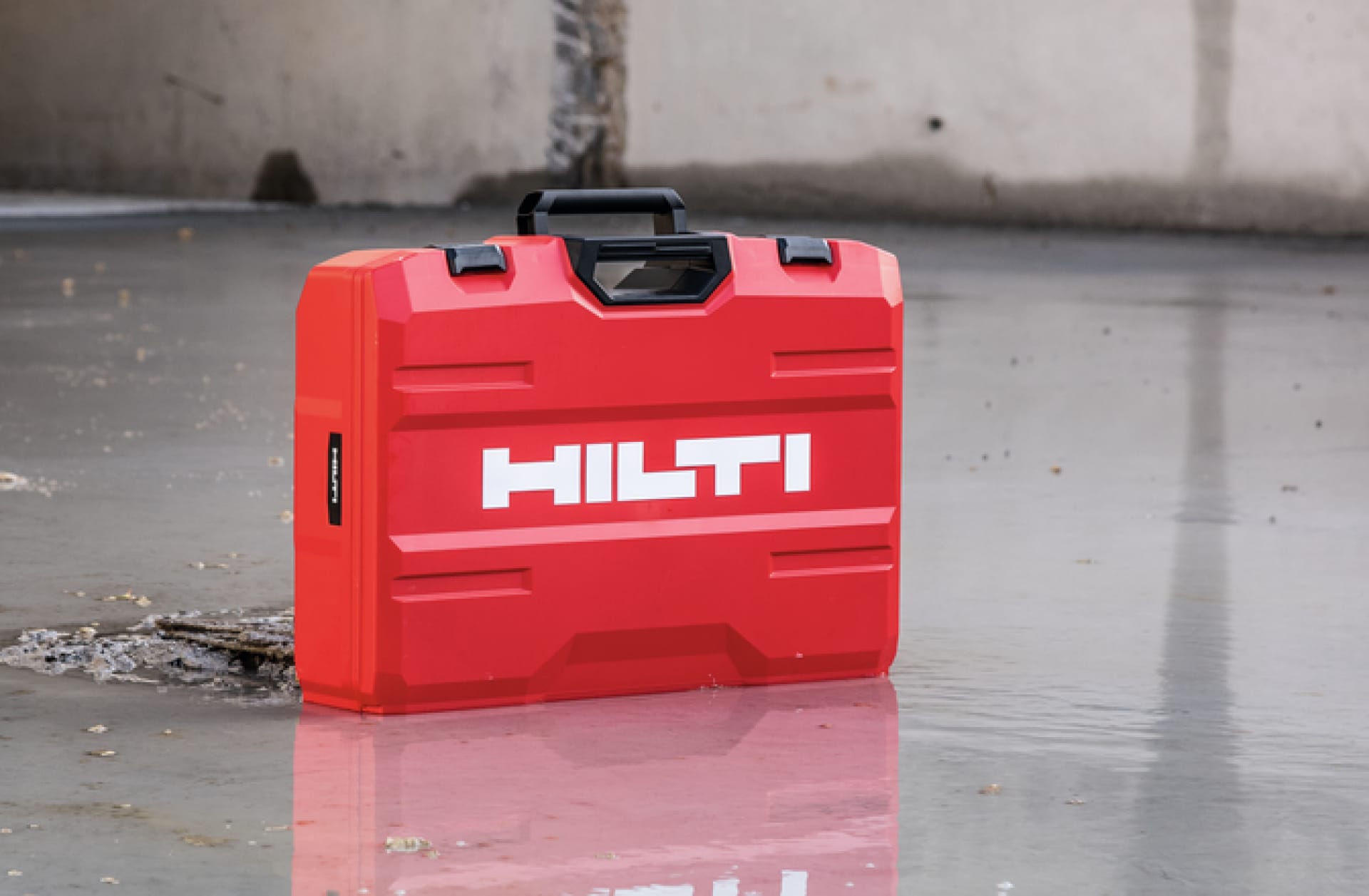 L'immagine è divisa in due aree: a sinistra un uomo solleva dallo scaffale una valigia Hilti rossa, a destra sono raffigurate tre apparecchiature in scala di grigi, davanti alle quali si trova un cerchio rosso con al centro il simbolo dell'euro bianco .